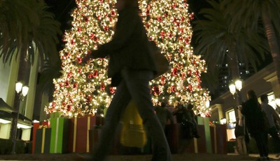 
              In this Thursday, Dec. 20, 2012, photo, a holiday shopper walks past a large Christmas tree at Fashion Island shopping center in Newport Beach, Calif. Holiday shopping, strong auto sale